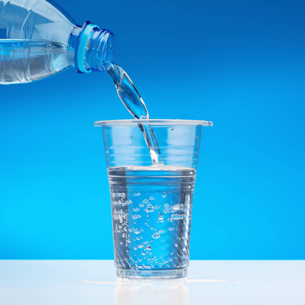 Sparkling water flows from bottle into glass. Blue background, copy space.