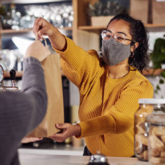 Shot of a woman wearing a mask while serving a customer in a cafe